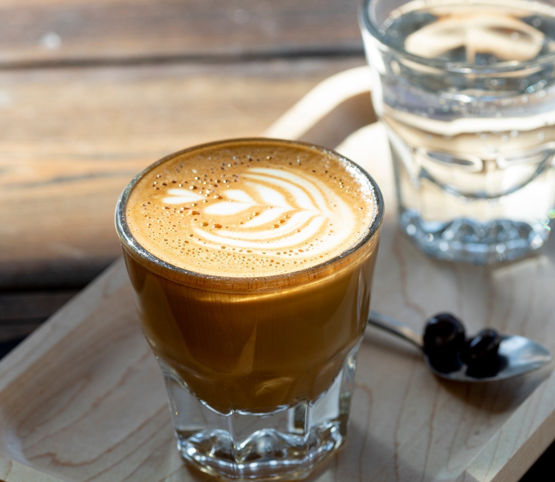A Gibraltar sitting on a wooden board - The Gibraltar is an espresso drink with 2 shots and a little bit of foamed milk