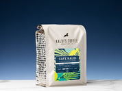 A 2lb bag of Cafe Kaldi sits on marble countertop in front of an uplit blue wall