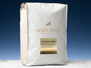 A 5lb bag of Dancing Goats Blend sits on marble countertop in front of an uplit blue wall