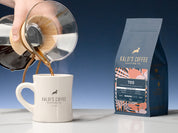 A 12oz bag of 700 beside a diner mug as coffee is being poured from a chemex into the mug, on a marble counter
