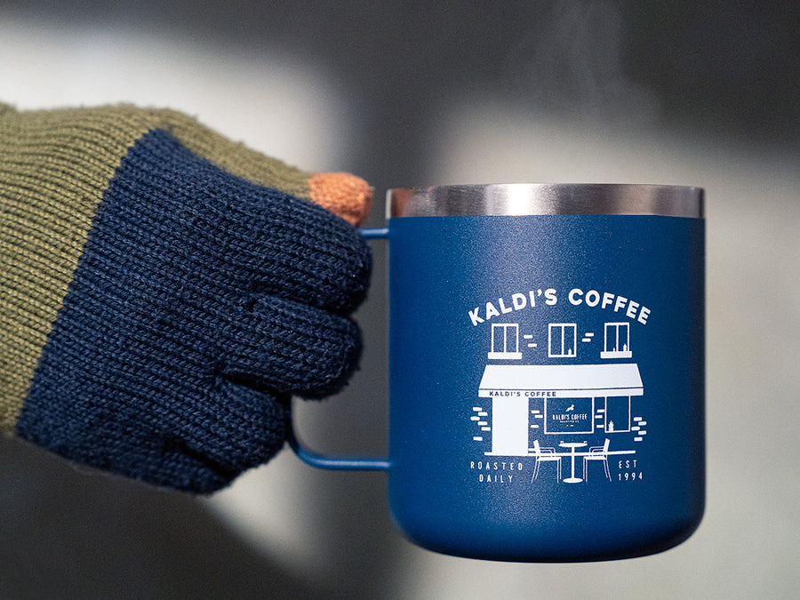 A gloved hand holds a steaming blue camper mug