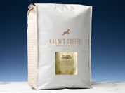 A five pound bag of Colombia Community sits on a white marble countertop, in front of an uplit blue wall.