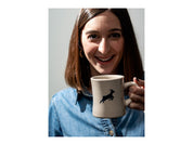 A woman smiles as a Kaldi's diner mug is lifted to her lips, with the goat logo showing
