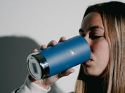 A woman sips from a lidless blue Klean Canteen, her shadow on the wall.