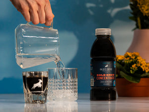 Pouring water into a glass with a Cold Brew Concentrate bottle to the side