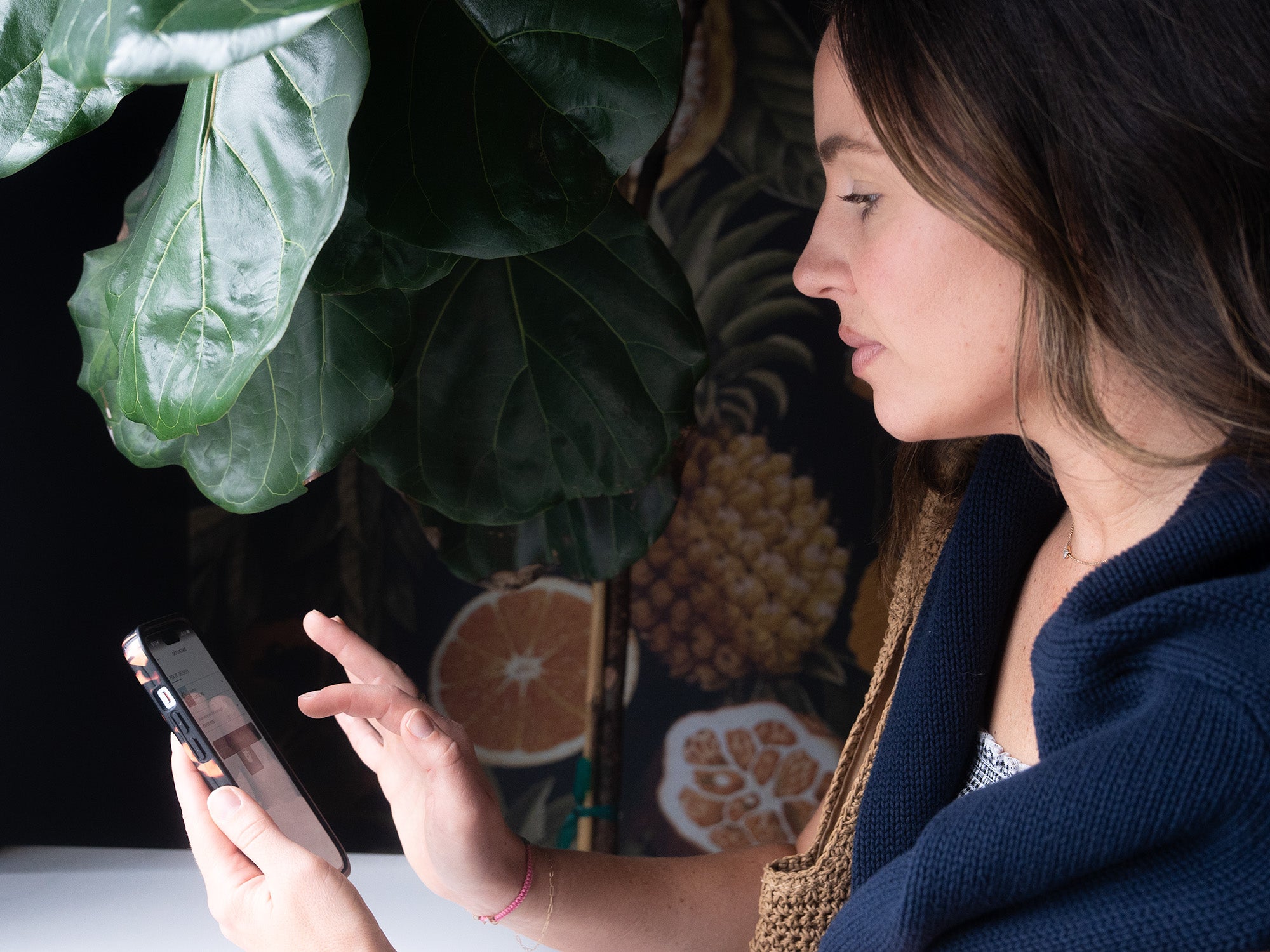 Woman using a smartphone with a decorative background featuring fruits and plants.