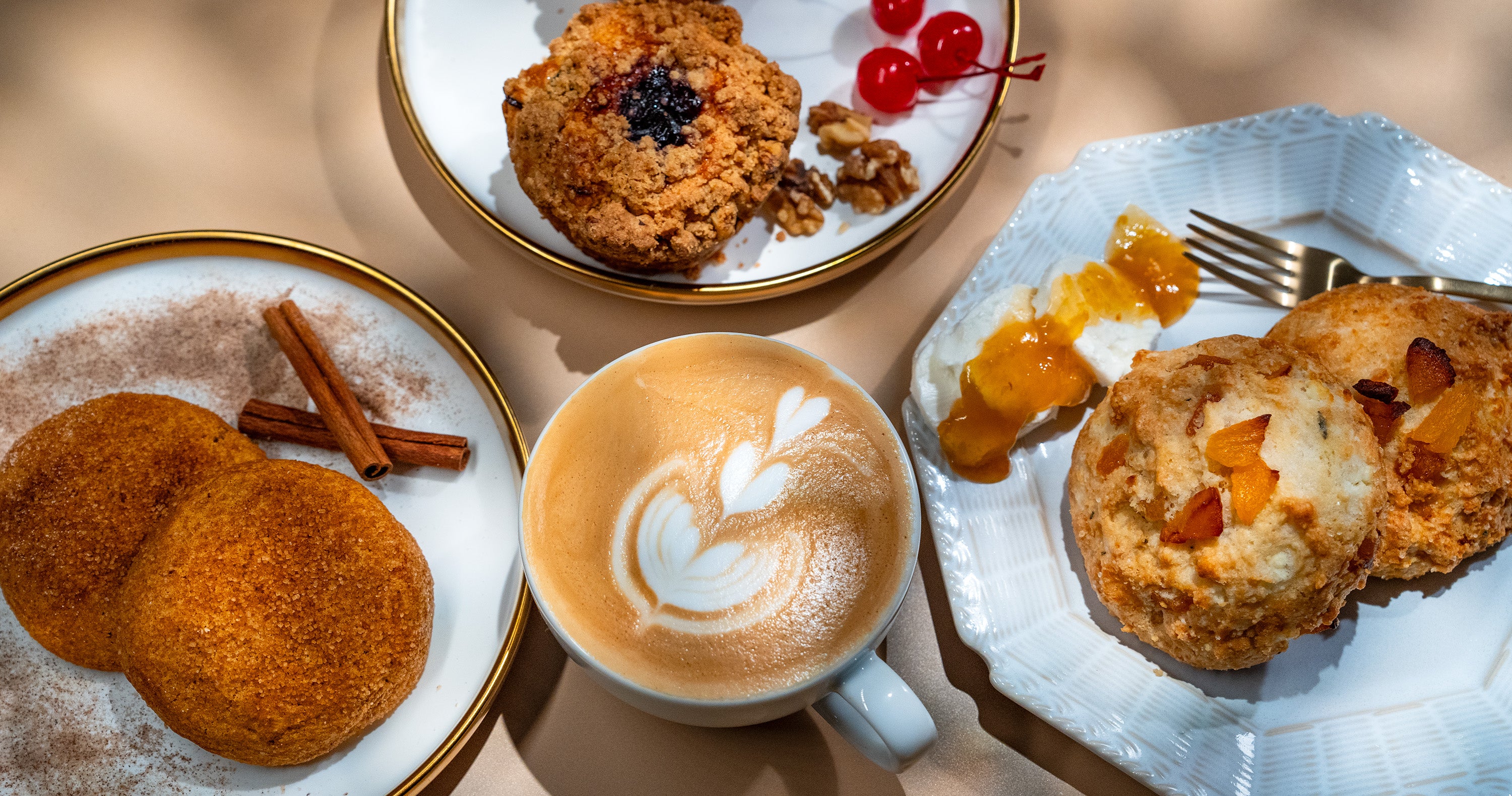 A smorgasbord of fall pastries sits on a golden tabletop with a latte