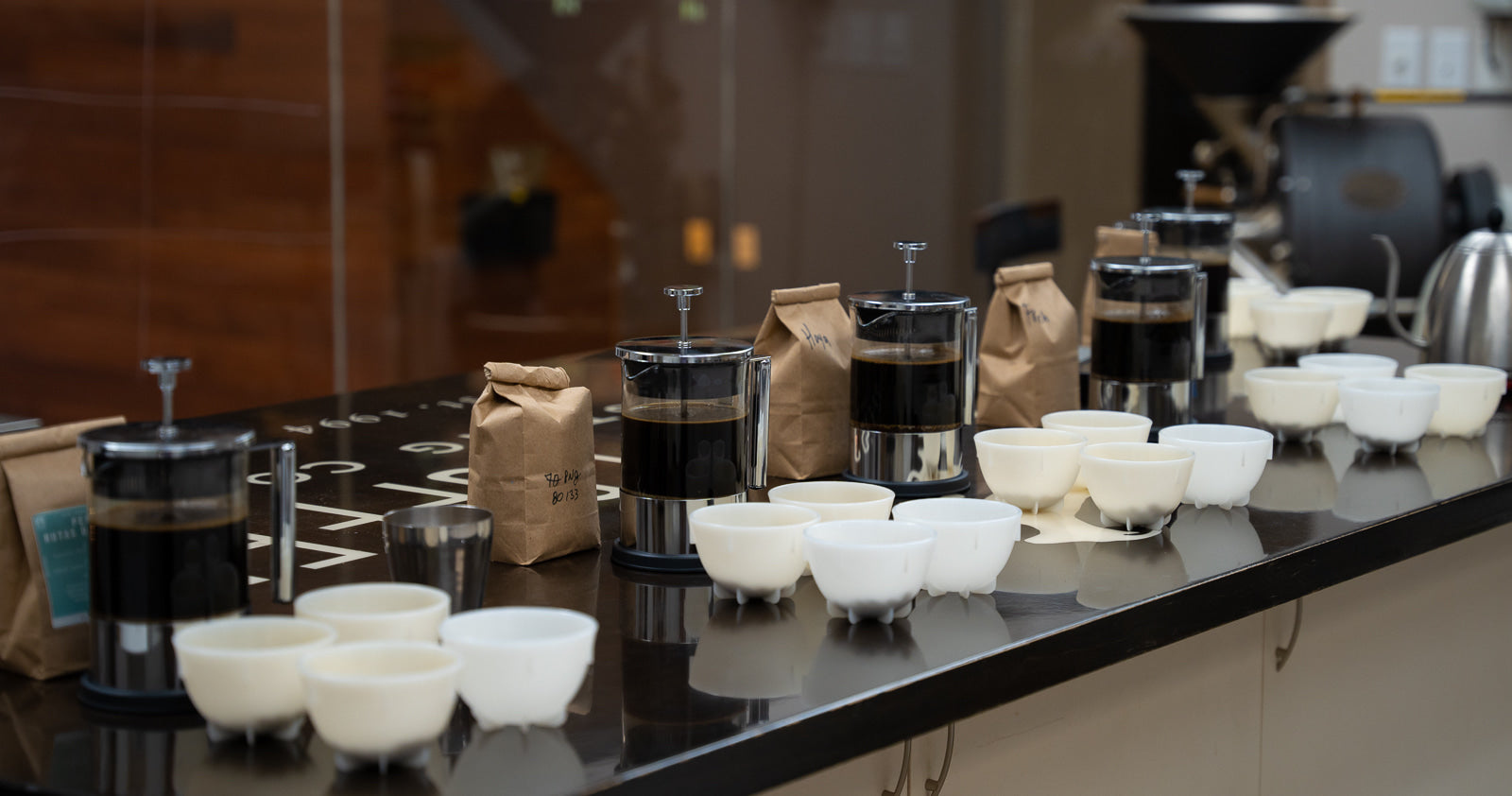 Cold brew coffee in French Presses next to coffee cupping bowls.
