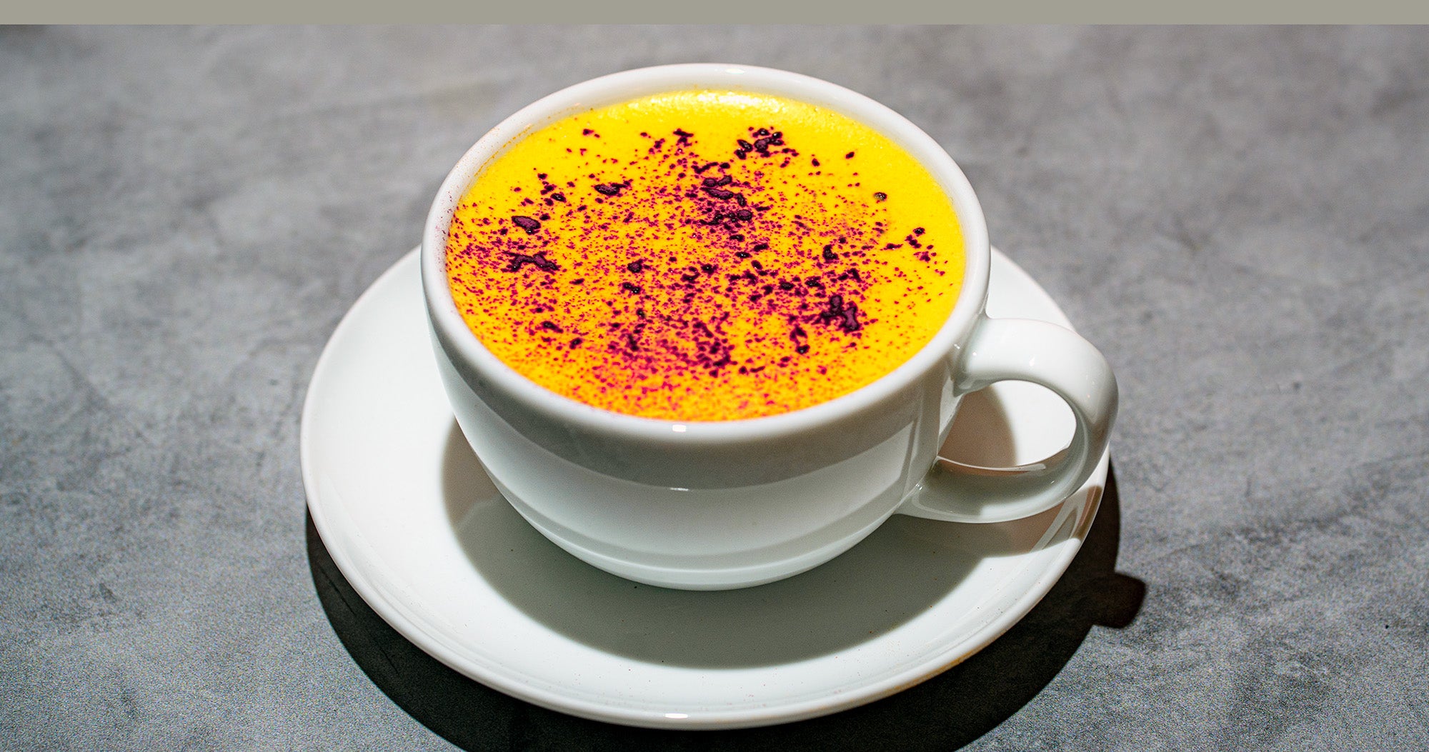 A bright yellow latte dusted with purple dragon fruit powder rests on concrete