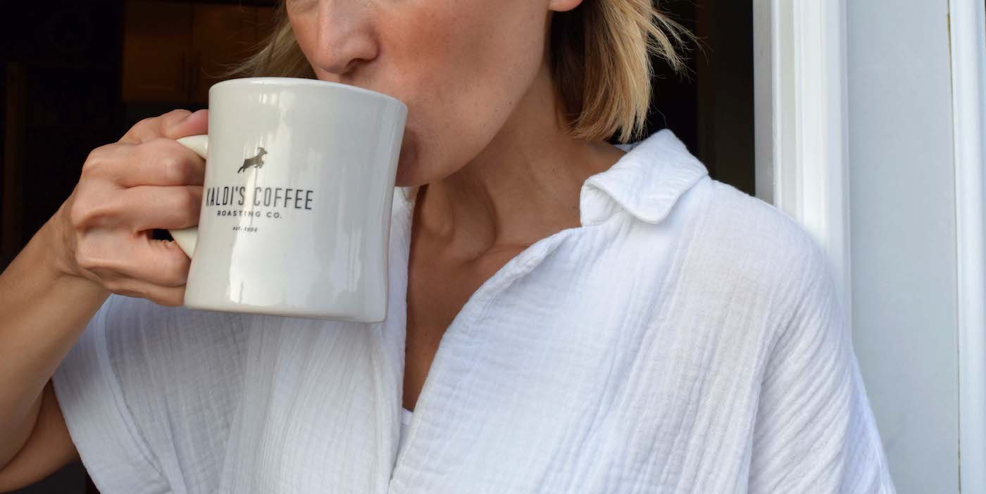 A woman taking a sip from a Kaldi's Coffee diner mug
