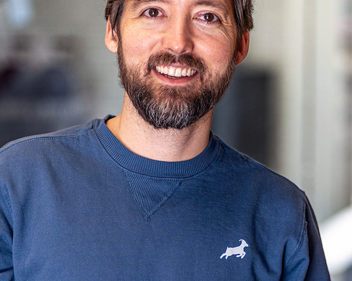 A smiling man with a beard wears a blue sweatshirt with Kaldi's goat logo over his left breast