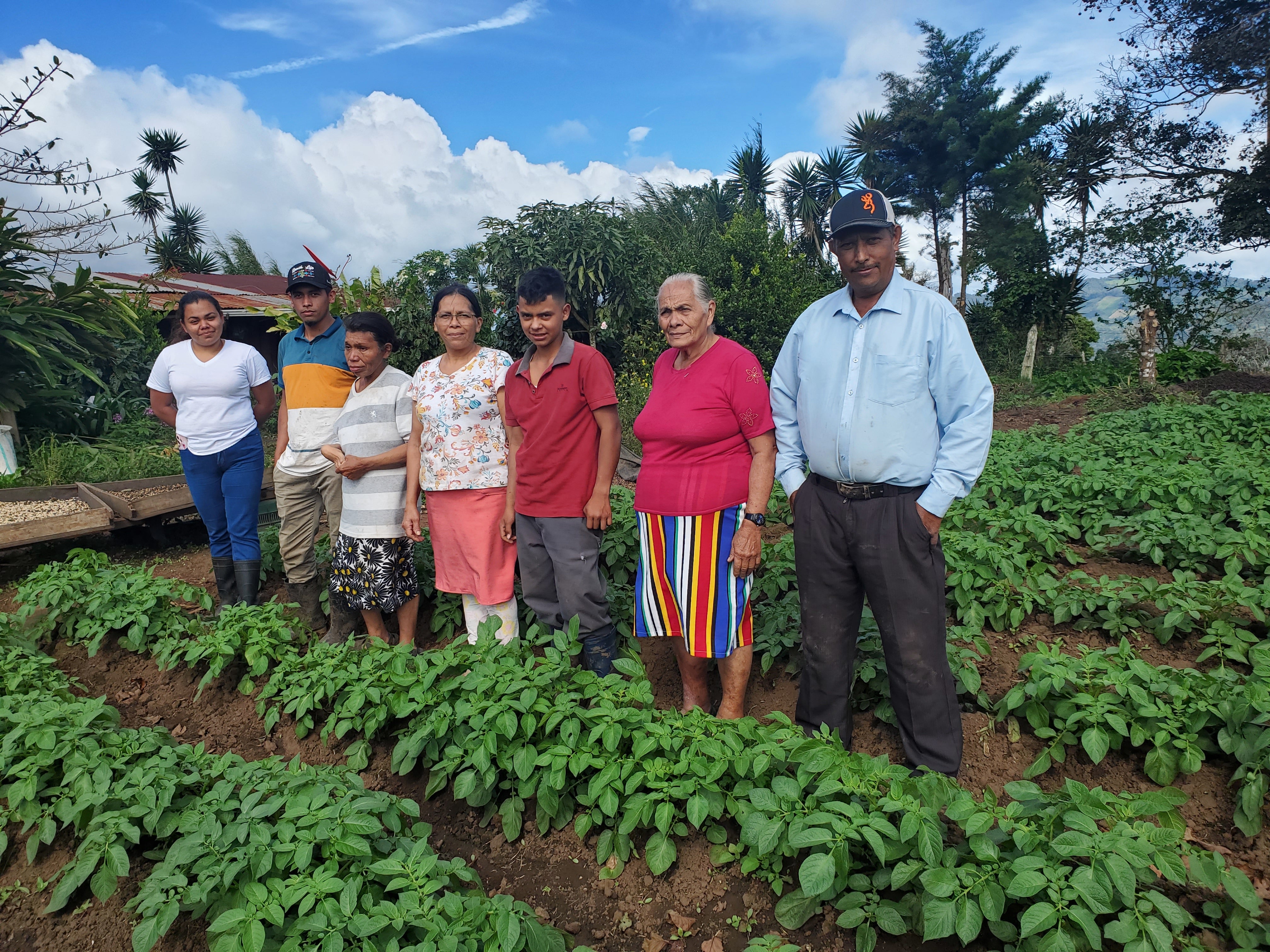 Group of people standing in a garden with rows of plants