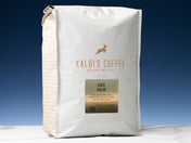 A 5lb bag of Cafe Kaldi sits on marble countertop in front of an uplit blue wall