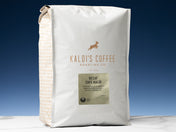 A 5lb bag of Decaf Cafe Kaldi sits on marble countertop in front of an uplit blue wall