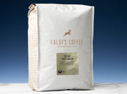 A 5lb bag of Decaf Cafe Kaldi sits on marble countertop in front of an uplit blue wall