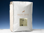 A 5lb bag of Decaf Highlander Grogg sits on marble countertop in front of an uplit blue wall