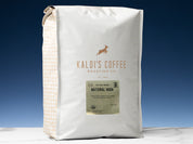 A 5lb bag of Fair Trade Organic Natural High sits on marble countertop in front of an uplit blue wall
