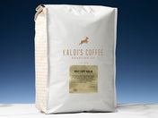 A 5lb bag of Half Caff Kaldi sits on marble countertop in front of an uplit blue wall