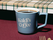 Blue mug with 'Kaldi's Coffee' text on a red tablecloth.