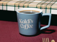 Blue mug with 'Kaldi's Coffee' text on a red tablecloth.