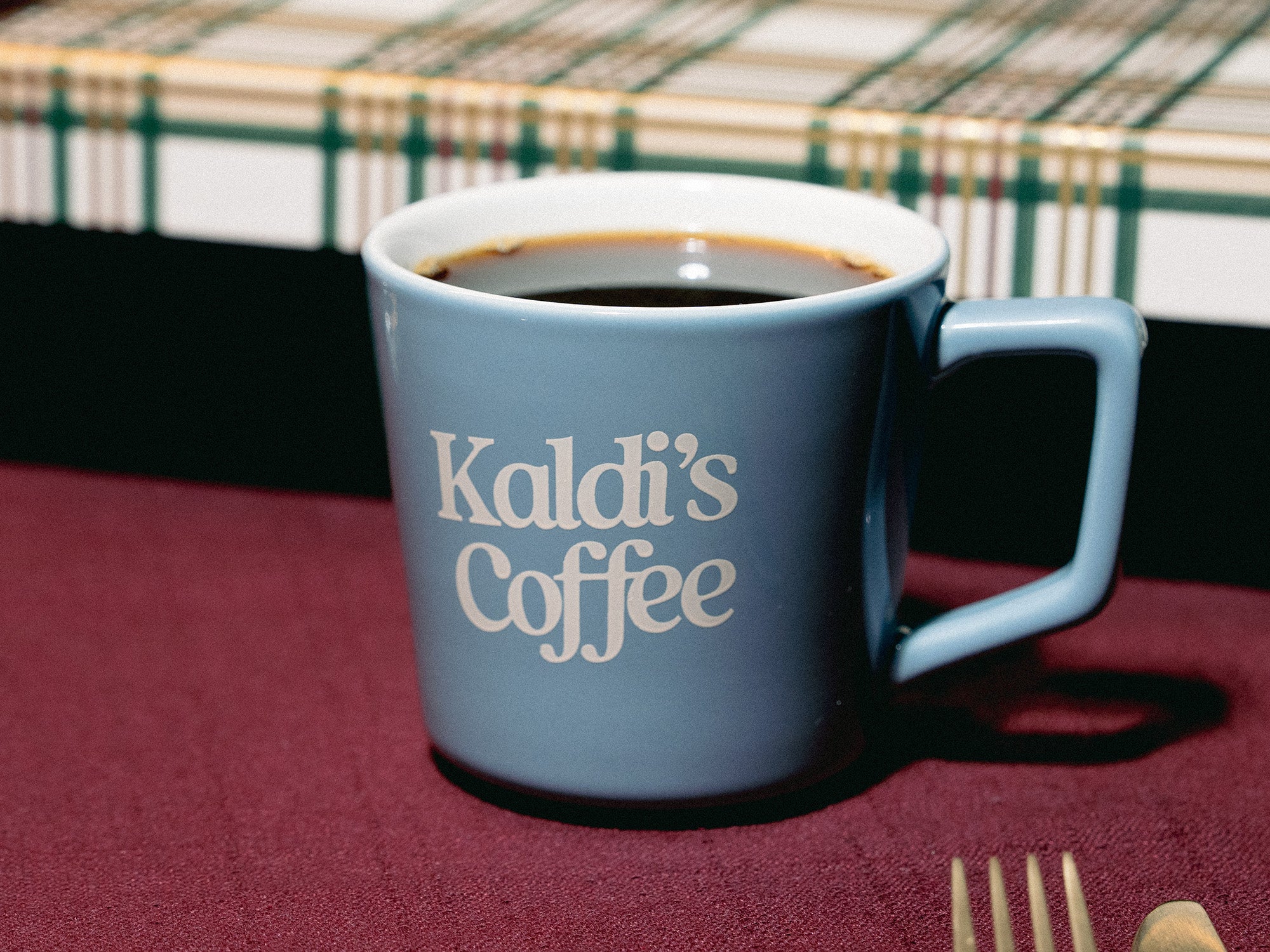 Blue mug with 'Kaldi's Coffee' text on a red tablecloth.