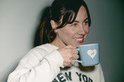 Woman holding a blue mug with a heart design against a plain background