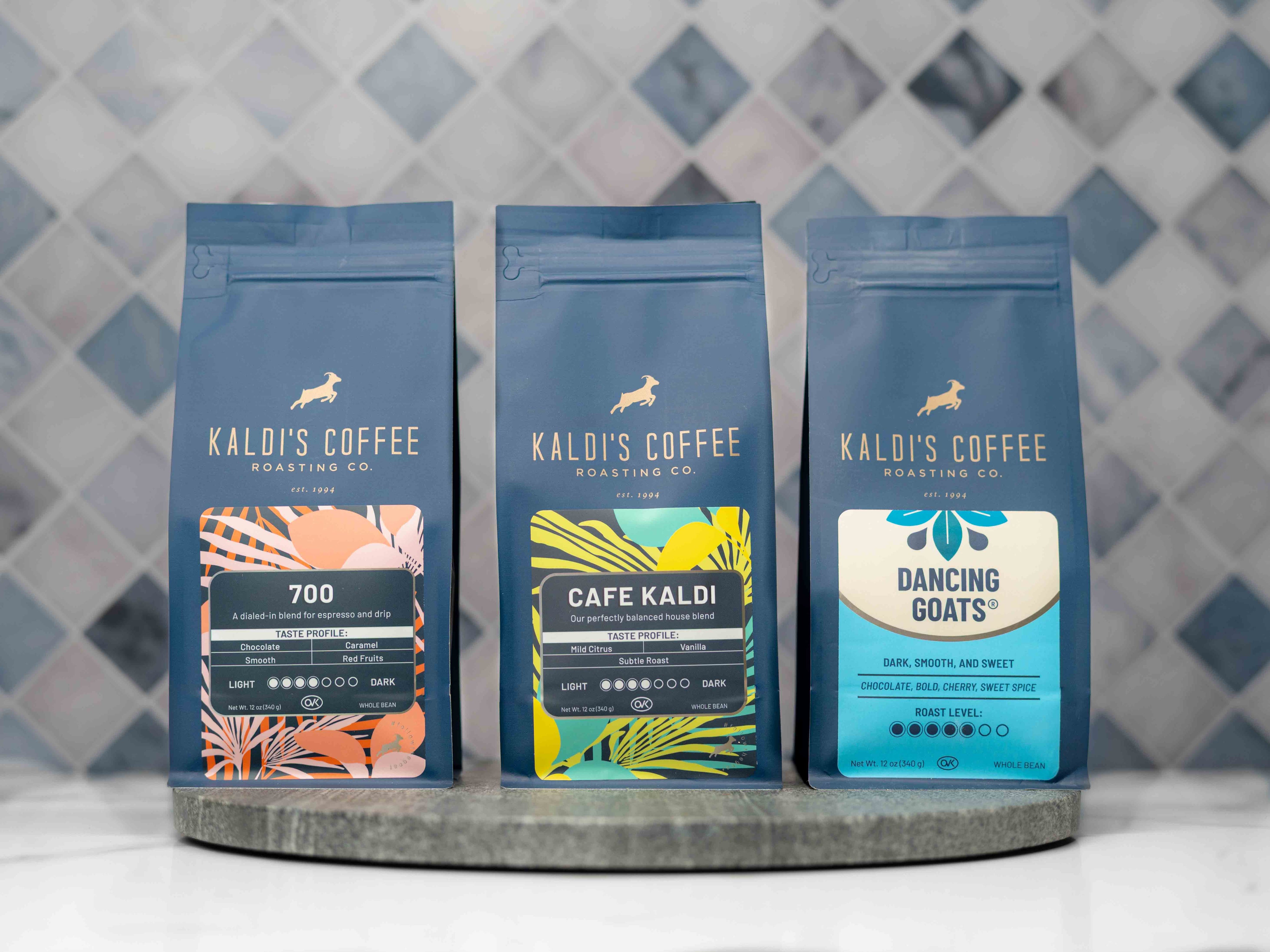 Three Kaldi's Coffee packages on a round metal tray with a patterned wall background.
