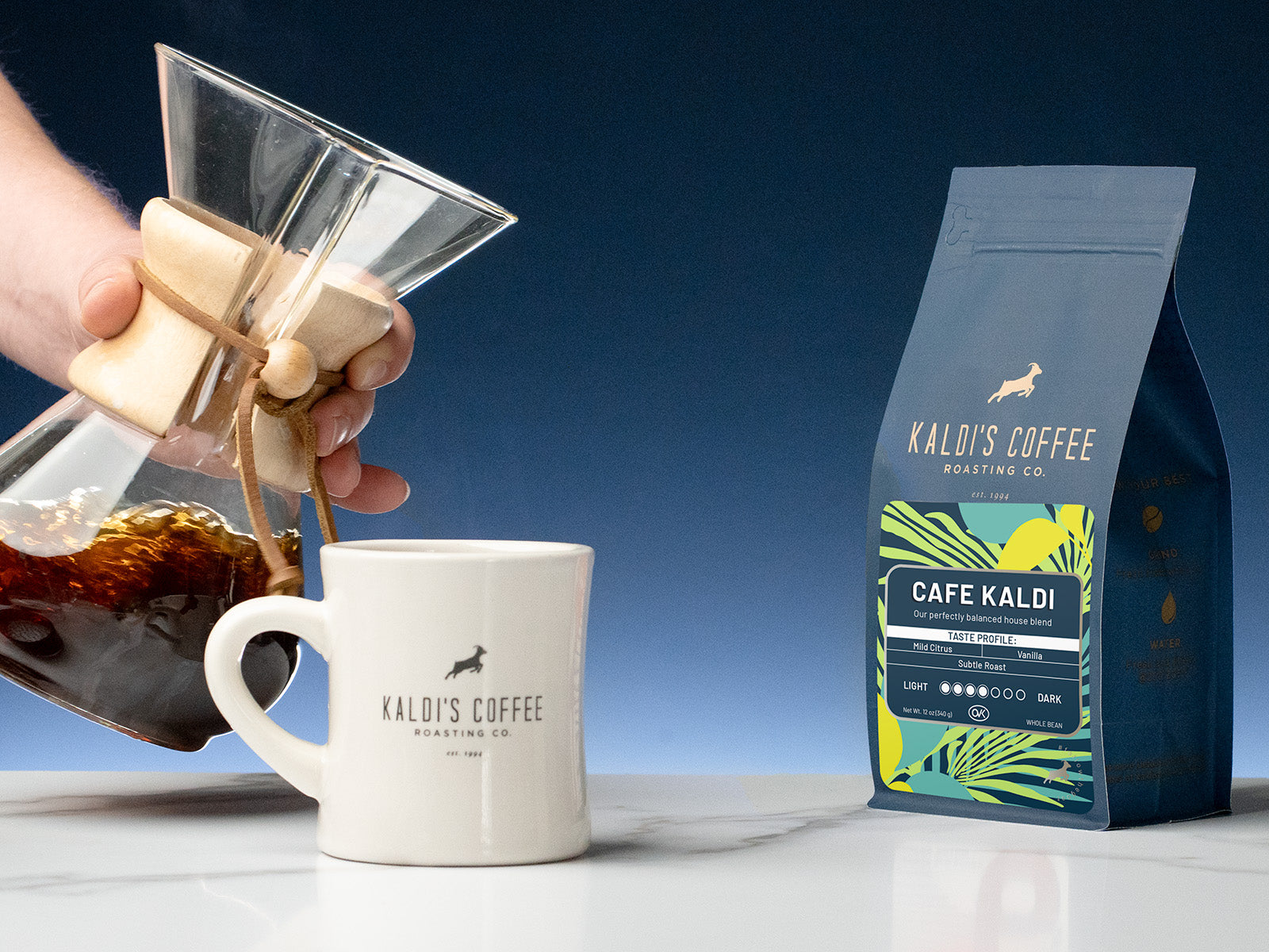 A 12oz bag of Cafe Kaldis beside a chemex being swirled above a Kaldi's diner mug