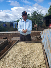 Juan Lucas holding coffee beans next to a truckload of coffee beans under a blue sky with clouds.