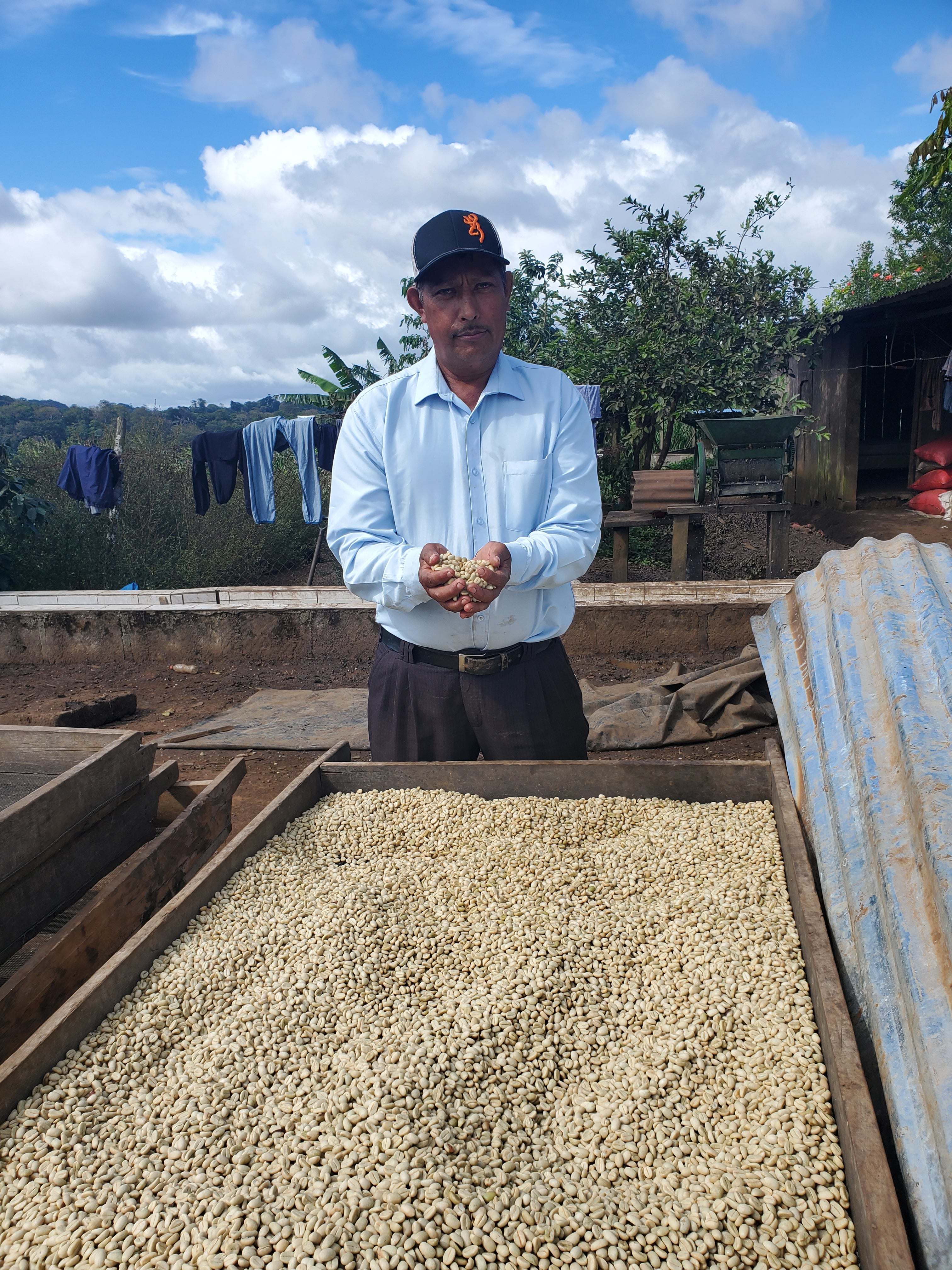 Juan Lucas holding coffee beans next to a truckload of coffee beans under a blue sky with clouds.