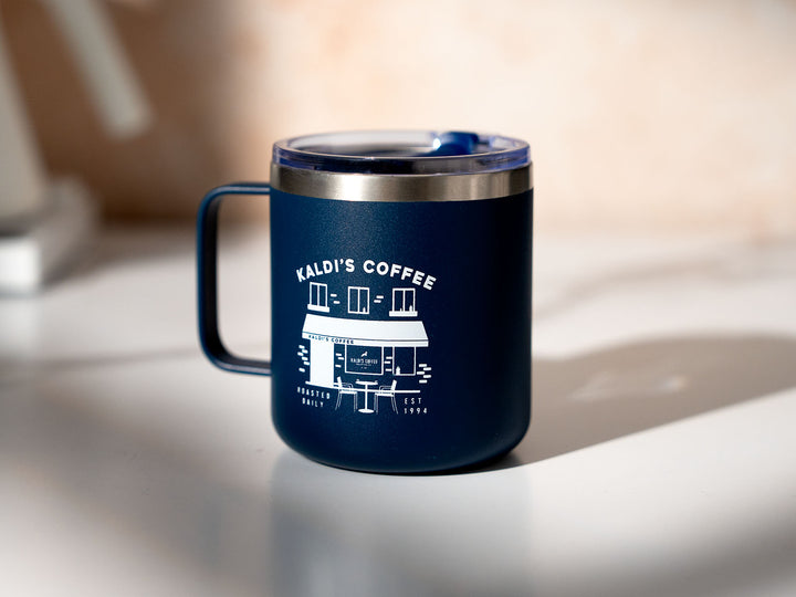 A blue camper mug with a cafe drawing sits on a counter