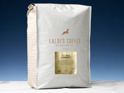 A five pound bag of Colombia Community sits on a white marble countertop, in front of an uplit blue wall.