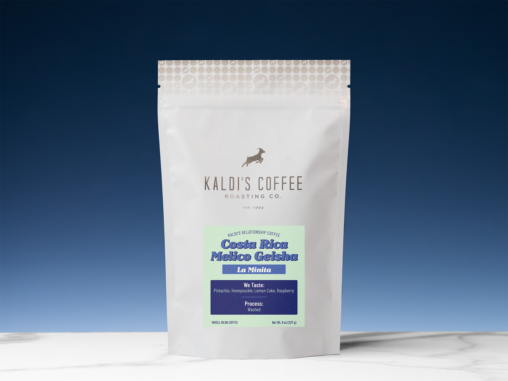 An 8oz pouch of Costa Rican coffee from La Minita sits on a white marble countertop, in front of a gradient blue background that is light blue and ascends into dark blue.