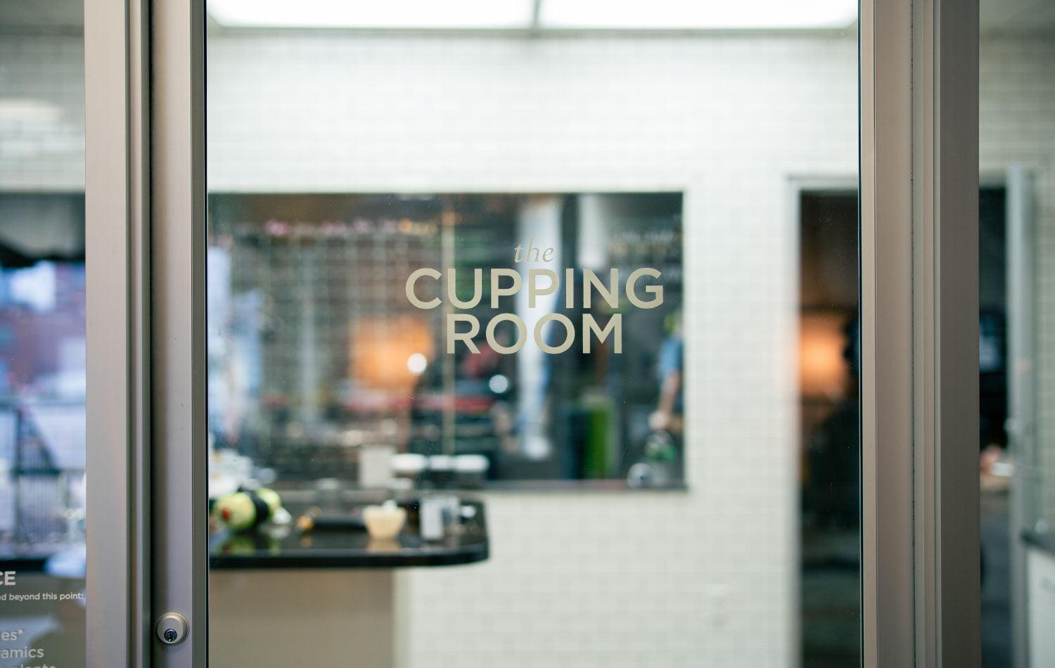 Glass door with 'The Cupping Room' sign inside a modern interior setting.