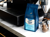 Styled Image of 12 ounce bag of Dancing Goats blend next to an espresso machine and a coffee grinder.