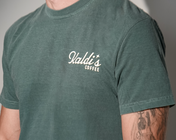 A close-up of a person wearing a faded dark green t-shirt with a white graphic that reads 'Kaldi's Coffee'.