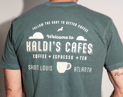 A back view of a muted teal-green graphic T-shirt with white printed text.