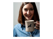 A woman smiles as a Kaldi's diner mug is lifted to her lips, with the goat logo showing