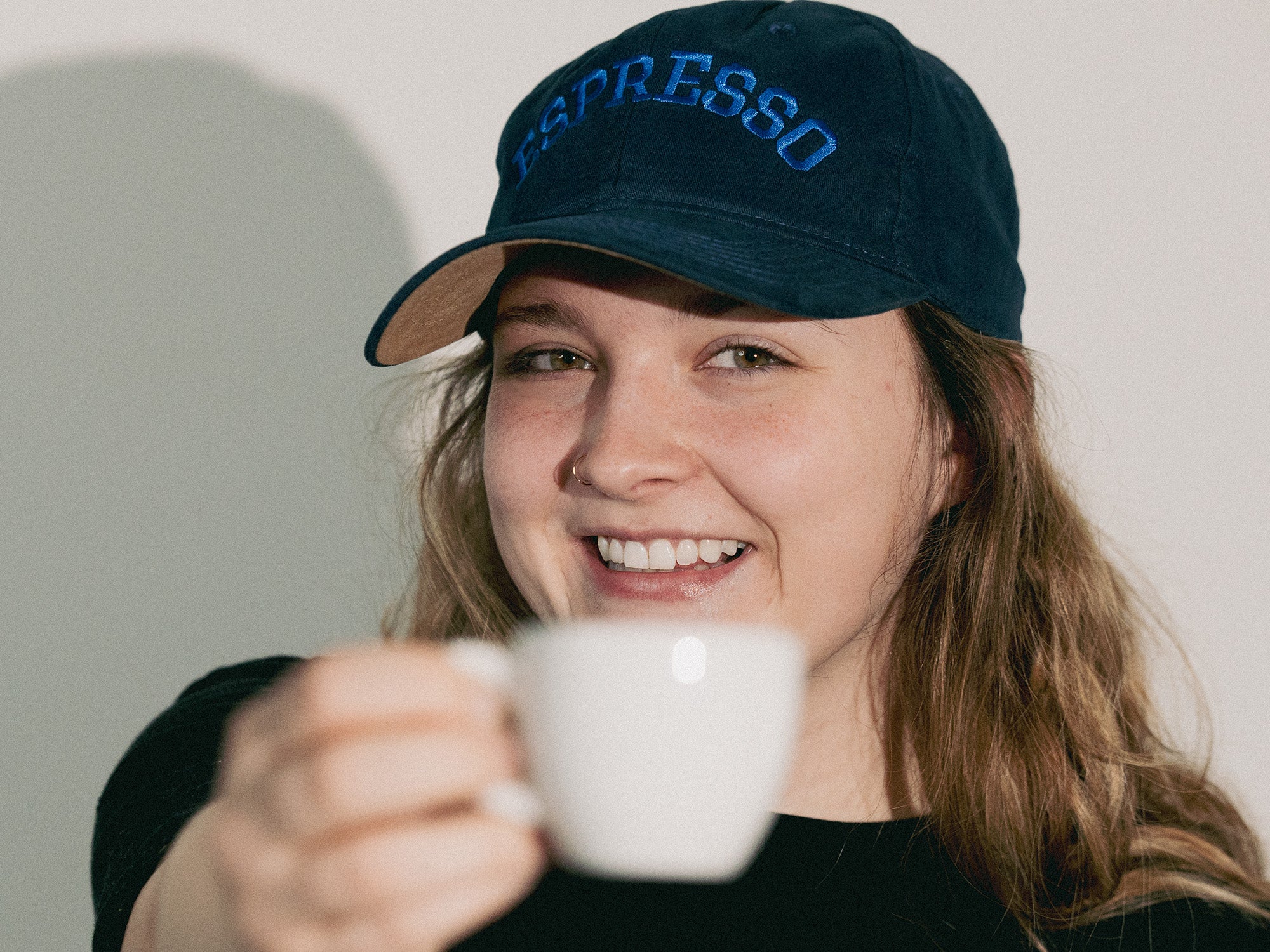 Person wearing a navy blue cap with 'Espresso' text, holding a white cup.
