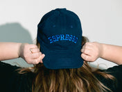 Person wearing a navy blue cap with 'ESPRESSO' text, holding it behind their head against a plain background.