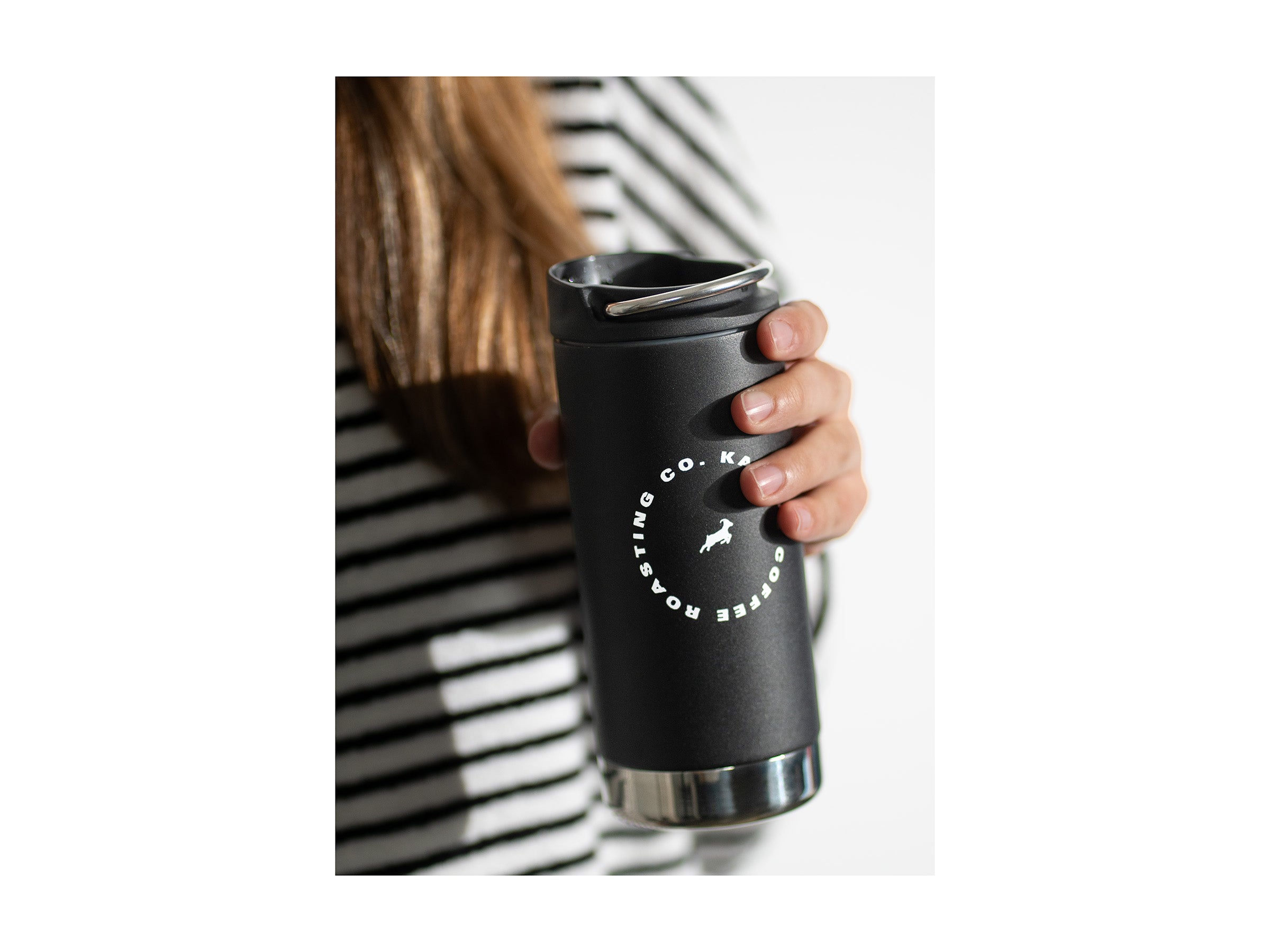 A hand holds a black Klean Canteen with white Kaldi's circle logo before sipping