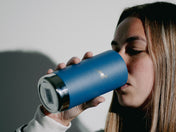 A woman sips from a lidless blue Klean Canteen, her shadow on the wall.