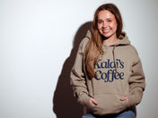 Model wearing a Kaldi's Coffee hooded sweatshirt in Tan