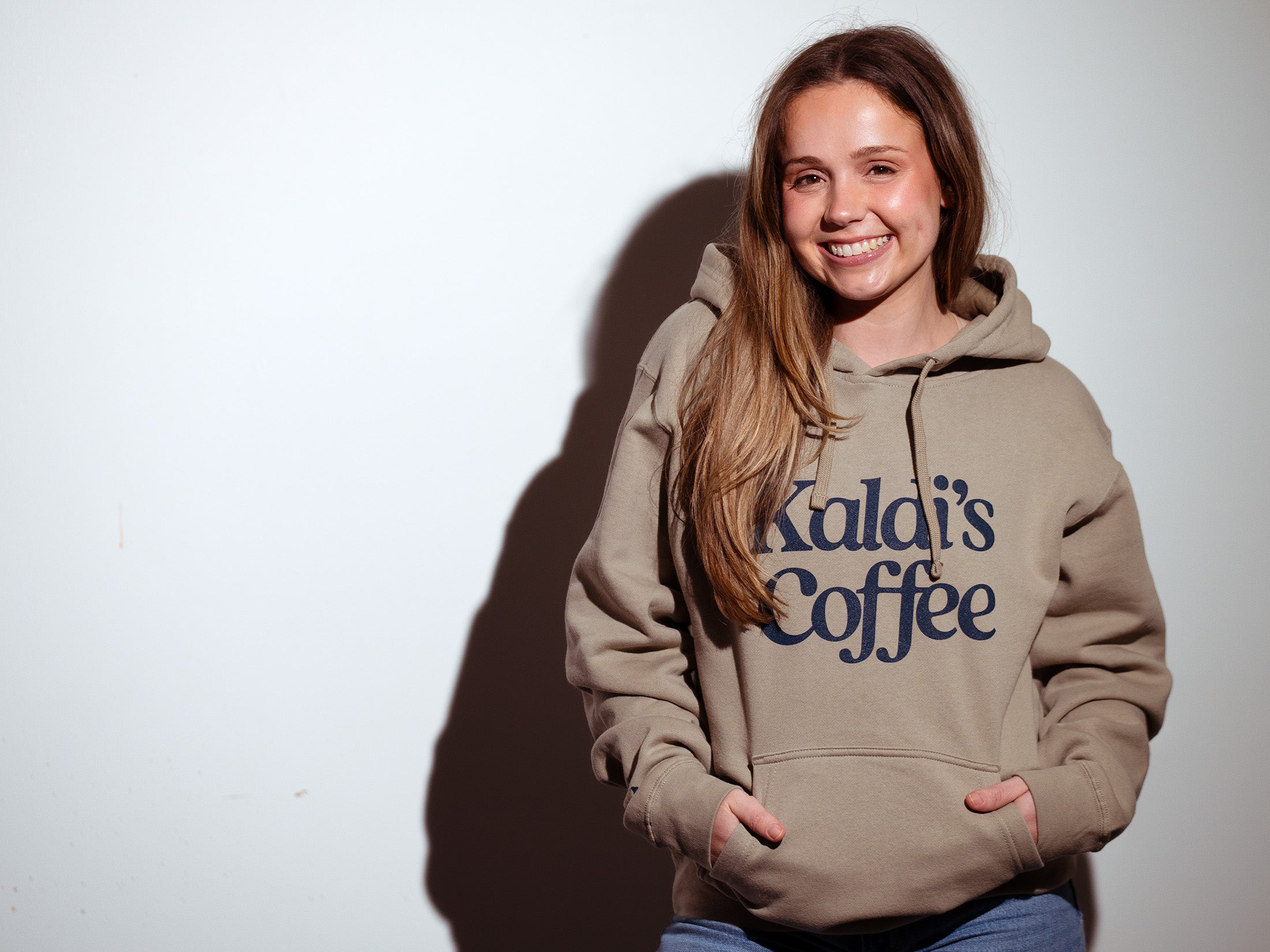 Model wearing a Kaldi's Coffee hooded sweatshirt in Tan
