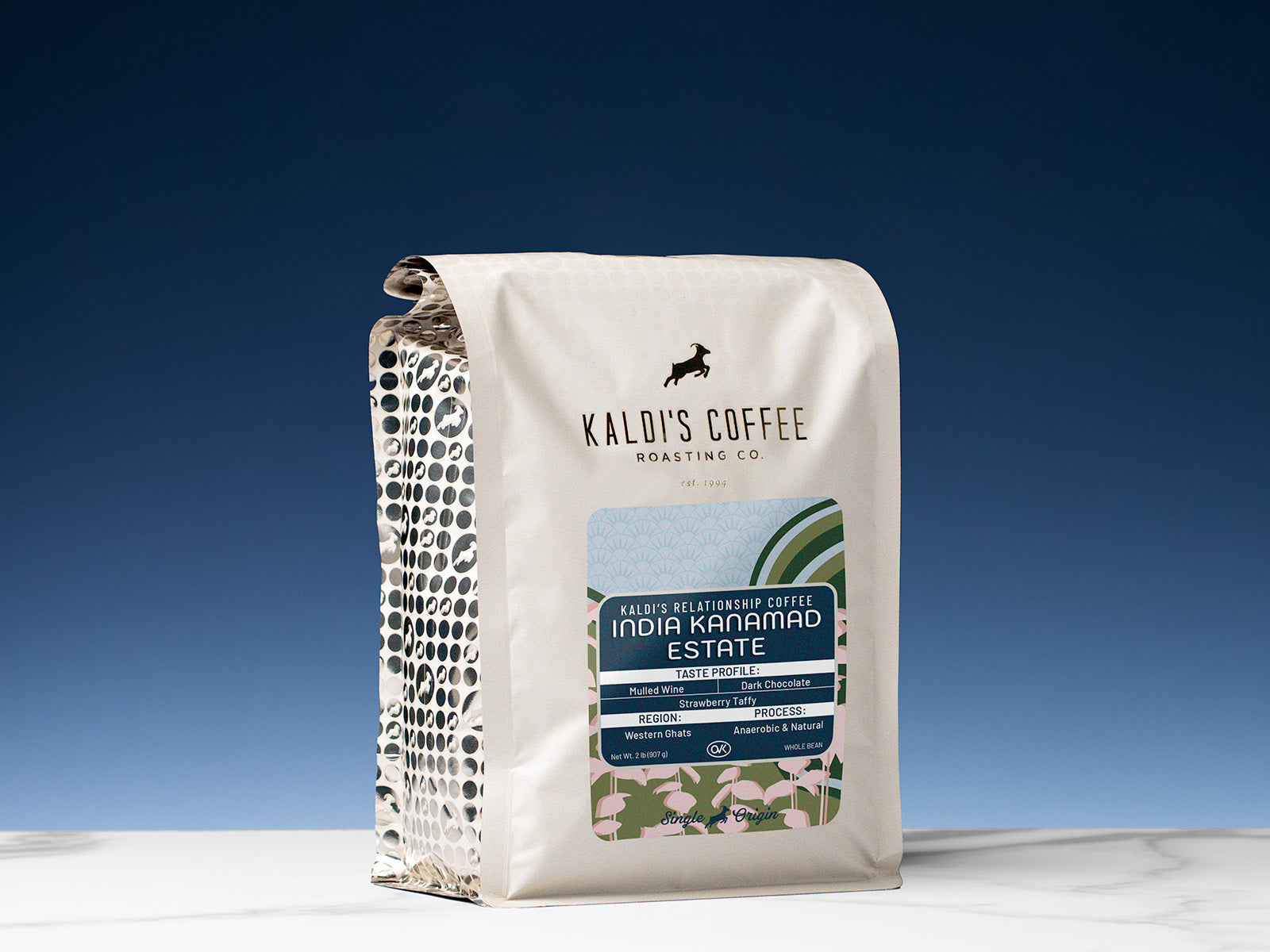A 2lb bag of India Kanamad Estate sits on a marble countertop in front of a blue wall lit from below