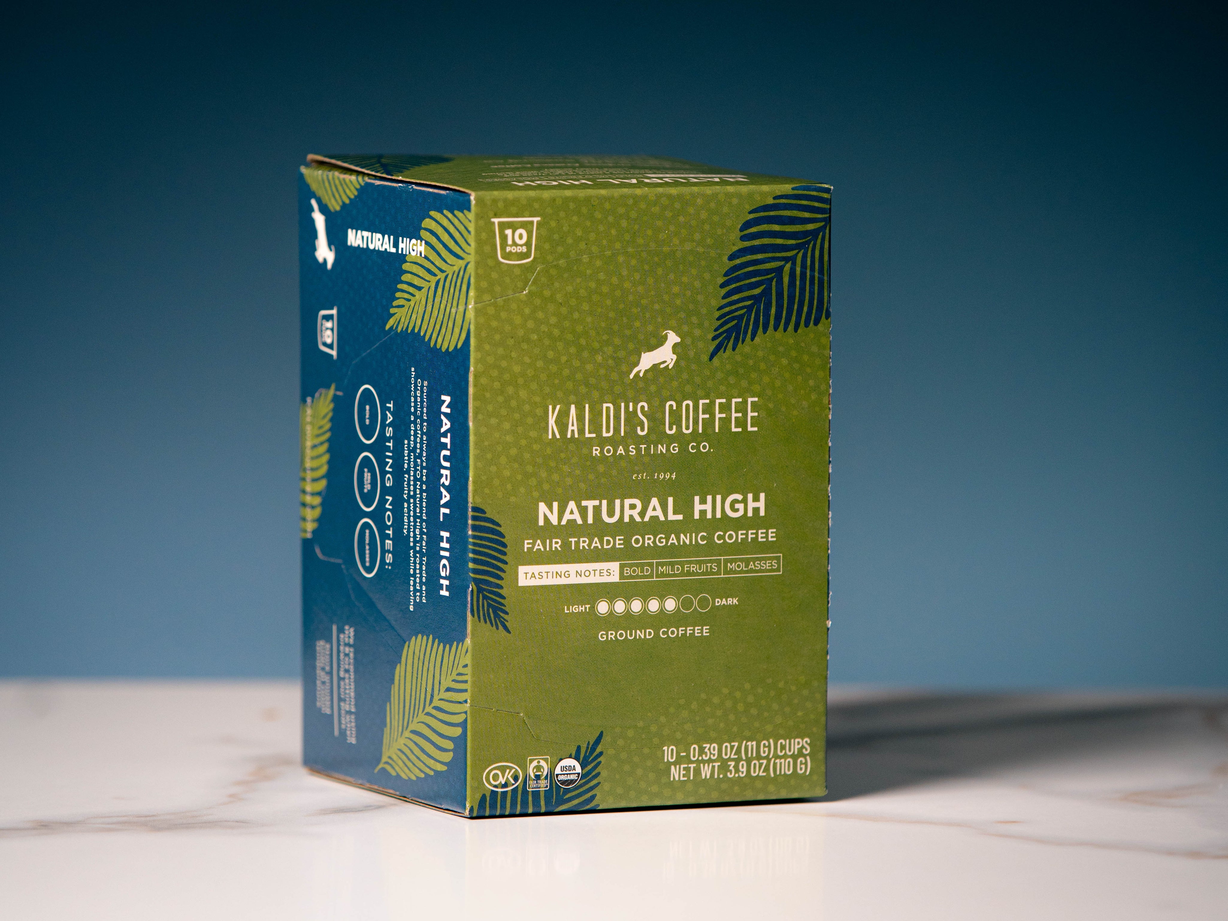 A box of Kaldi's Coffee Natural High Fair Trade Organic Coffee. The packaging is olive green with dark green palm leaf illustrations and a blue side panel.