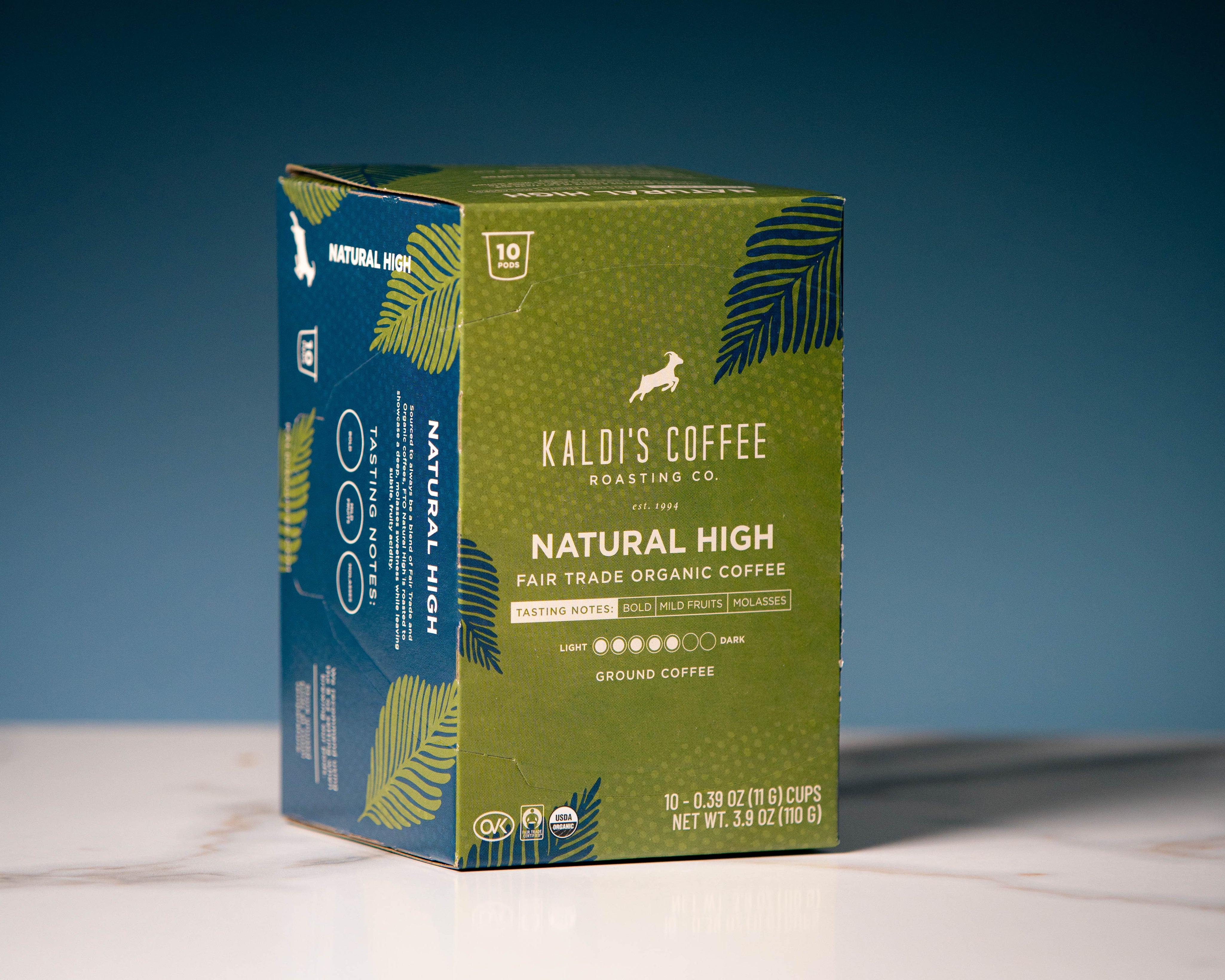 A box of Kaldi's Coffee Natural High Fair Trade Organic Coffee. The packaging is olive green with dark green palm leaf illustrations and a blue side panel.