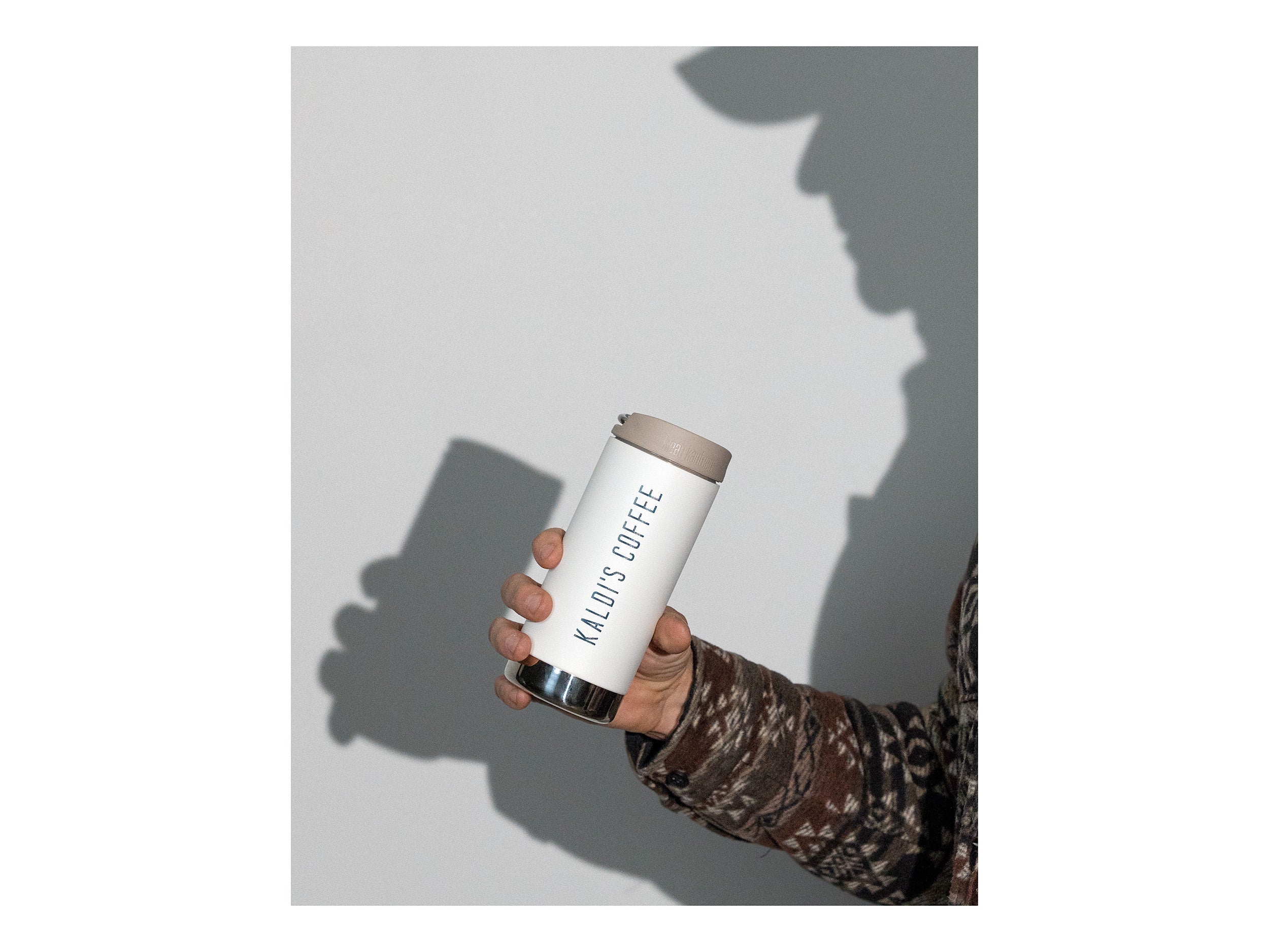 Hand holding a white tumbler with 'Kaldi's Coffee' branding against a light gray background