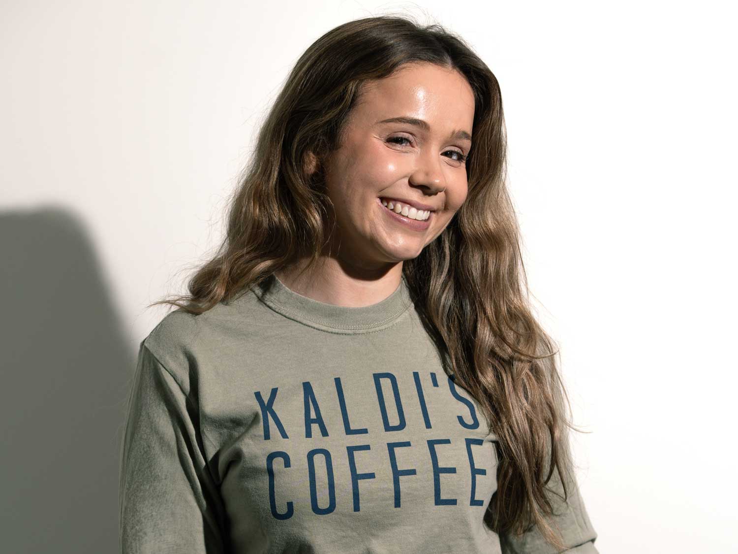 Woman wearing a green sweatshirt with 'Kaldi's Coffee' text on a white background