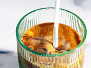 Pouring milk into a glass filled with coffee concentrate